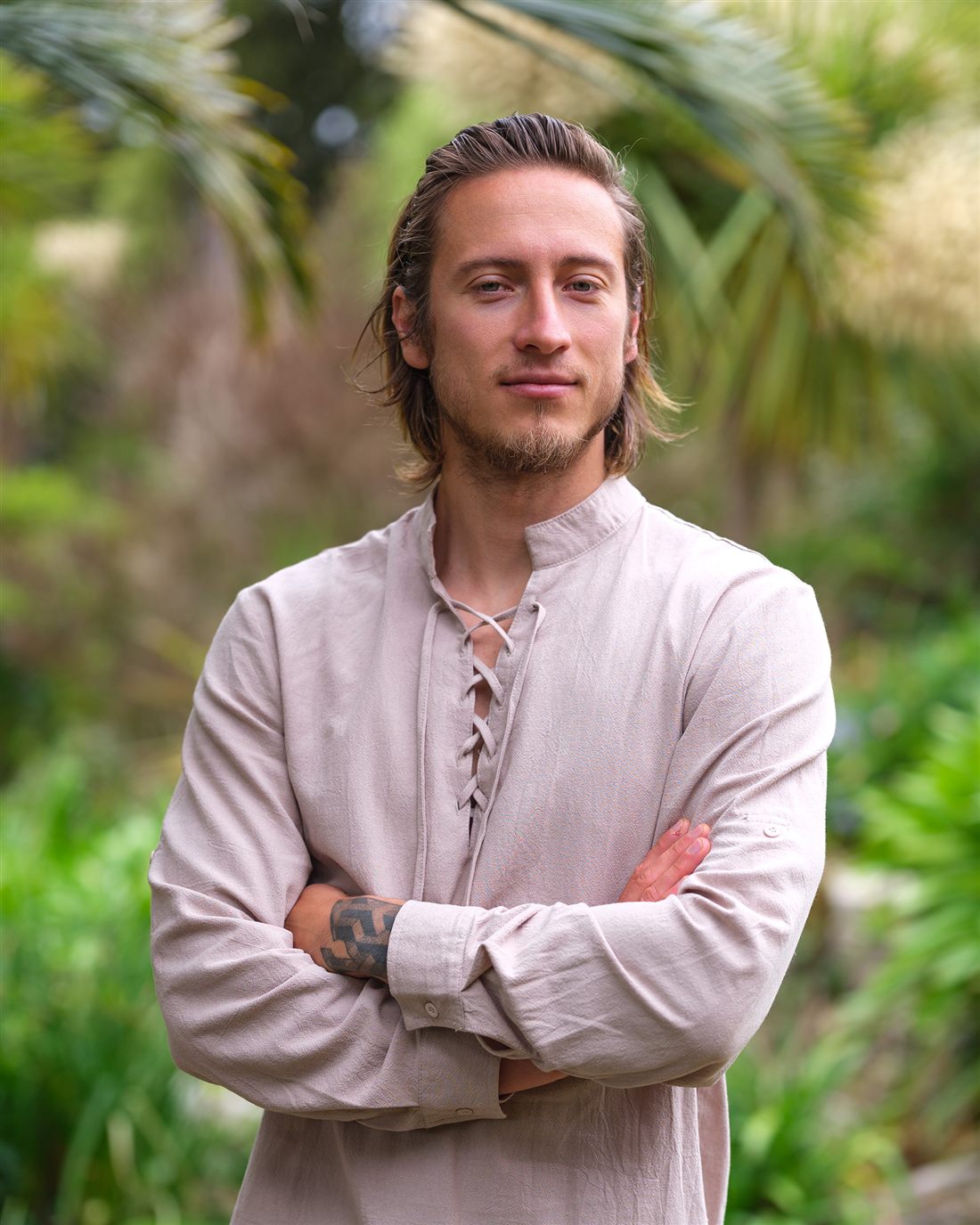 Karol standing outdoors, arms crossed, wearing a beige linen shirt